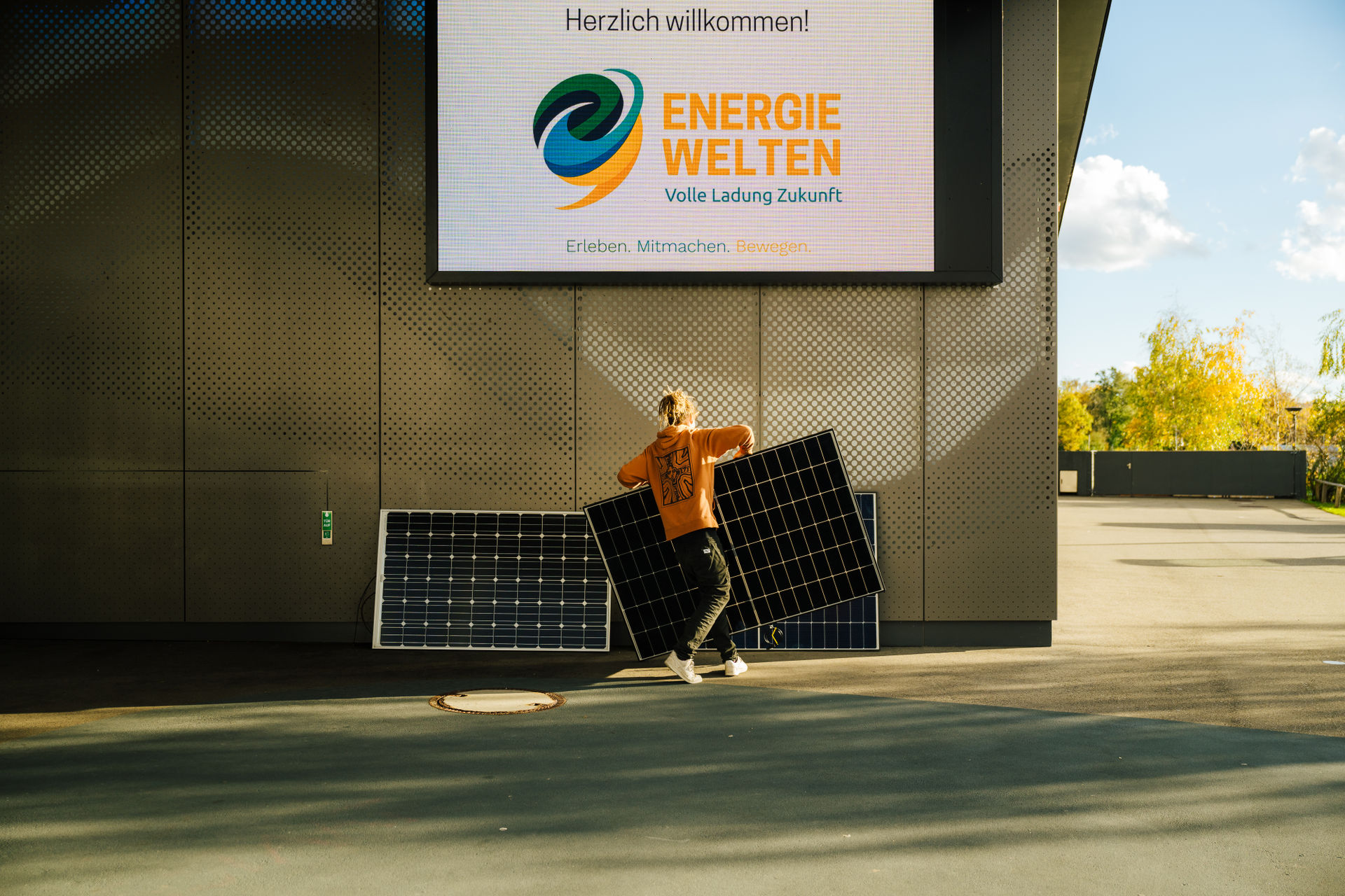 Entrada del Bodenseeforum de Constanza, con la pantalla dedicada a «ENERGIEWELTEN» y una persona apilando módulos solares delante de ella