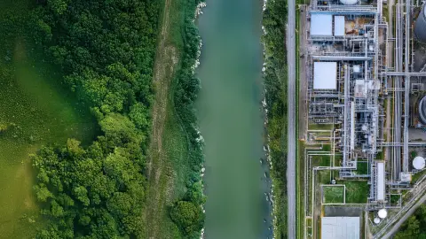 Flusslandschaft neben Industrieanlagen, symbolisiert Luftreinhaltung im GreenTech-Bereich