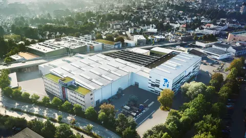 Aerial view of the EBZ site in Baden-Württemberg with several industrial halls and production buildings, surrounded by residential areas and green spaces.