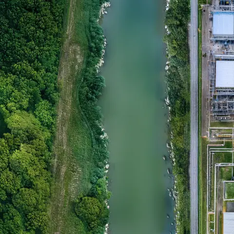 Flusslandschaft neben Industrieanlagen, symbolisiert Luftreinhaltung im GreenTech-Bereich